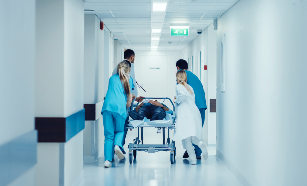 Fyra sjukvårdare springer i en korridor med en person i en sjukhussäng. 