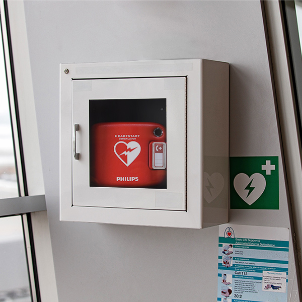 Defibrillator av märket Philips som sitter i ett skåp på en vägg inomhus.