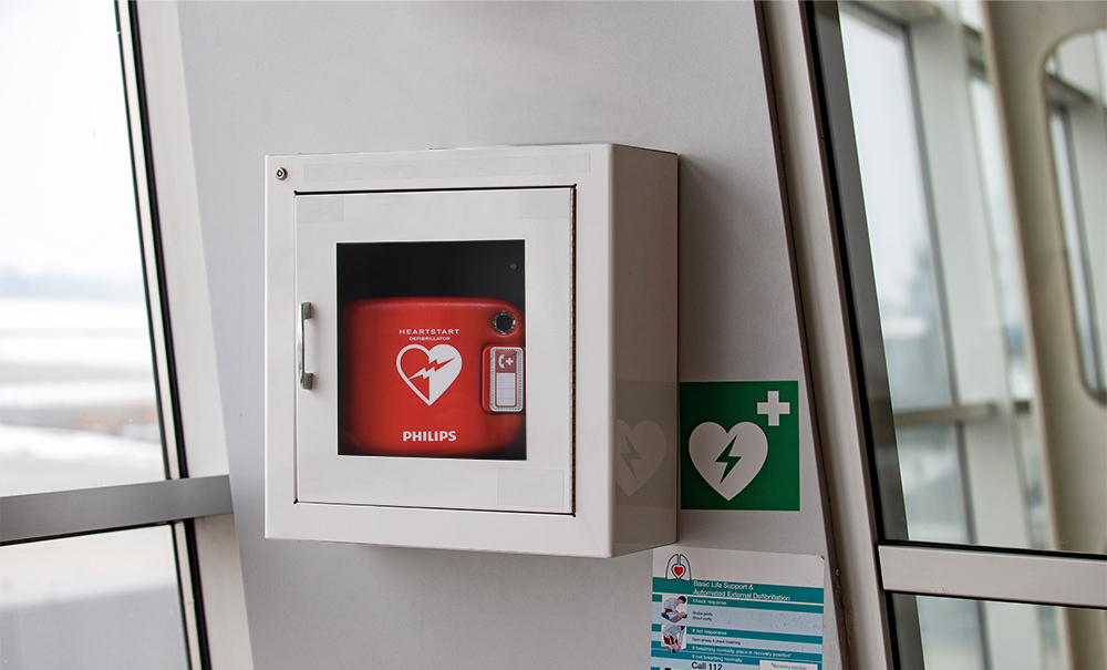 Defibrillator av märket Philips som sitter i ett skåp på en vägg inomhus.