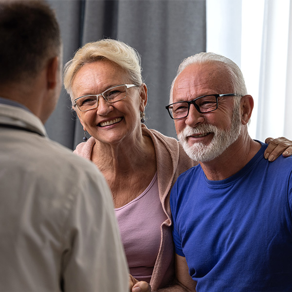 Friskt leende äldre par känner sig glada över goda nyheter vid läkarbesöket.