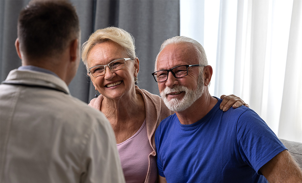 Glad äldre man och kvinna pratar med en läkare om hjärtstopp under ett läkarbesök.