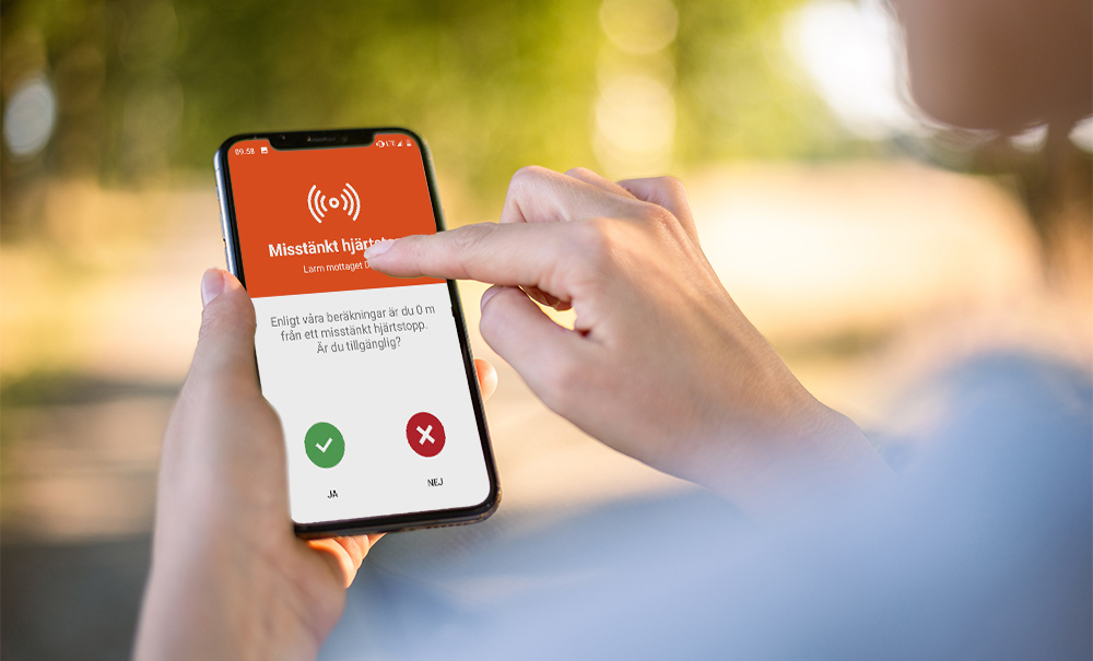 En mobiltelefon där skärmen visar ett inkommande larm om hjärtstopp i appen SMS livräddare. 