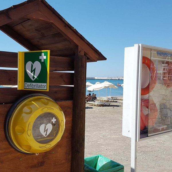 Gult väggskåp för hjärtstartare sitter upphängt vid en strand.