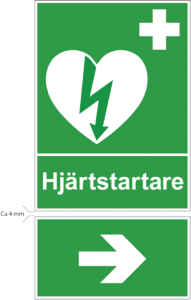 En grön skylt som visar symbolen för hjärtstartare samt har texten "hjärtstartare". Under denna skylt finns en till skylt i samma gröna nyans med en pil som är riktad åt höger. 